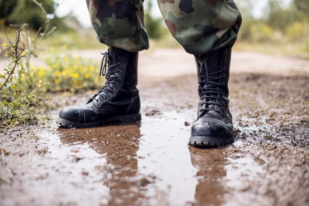 A military standing on dirt with army boots.