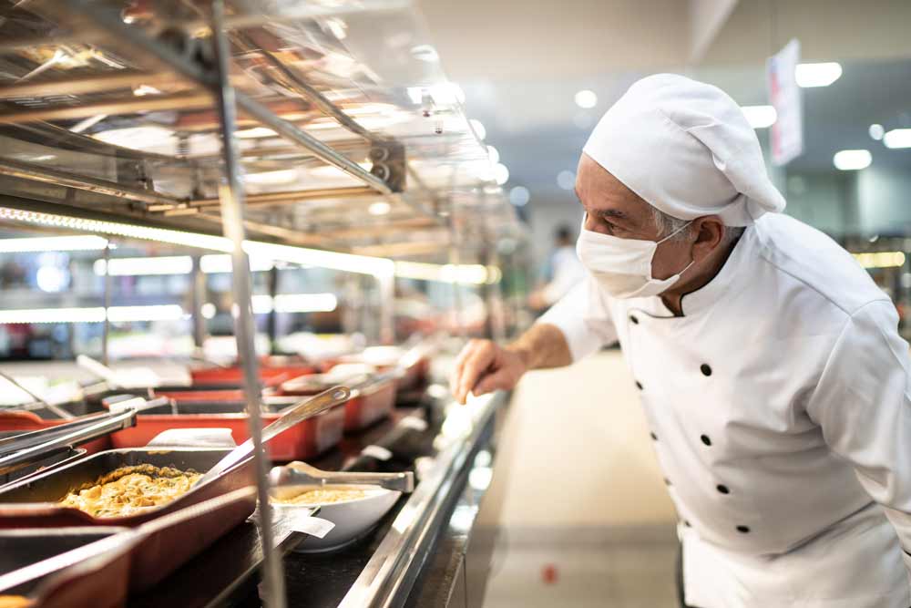 A chef with mouth protection looking at the food that's waiting to be served.